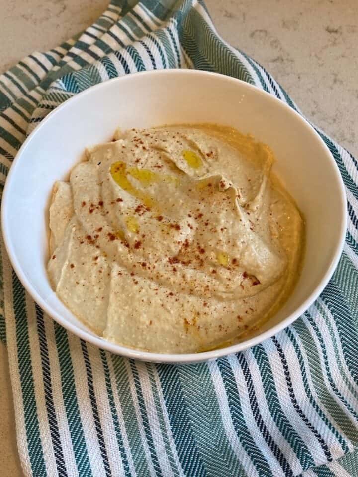 Bowl of simple classic hummus on a striped green towel