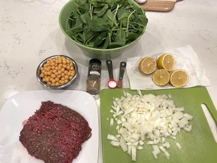 Ingredients including beef, onion, spinach, garbanzo beans and lemon for stew