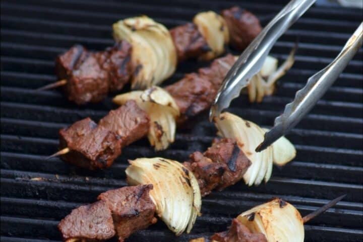 Tongs grabbing Armenian shish kebab on barbecue grill