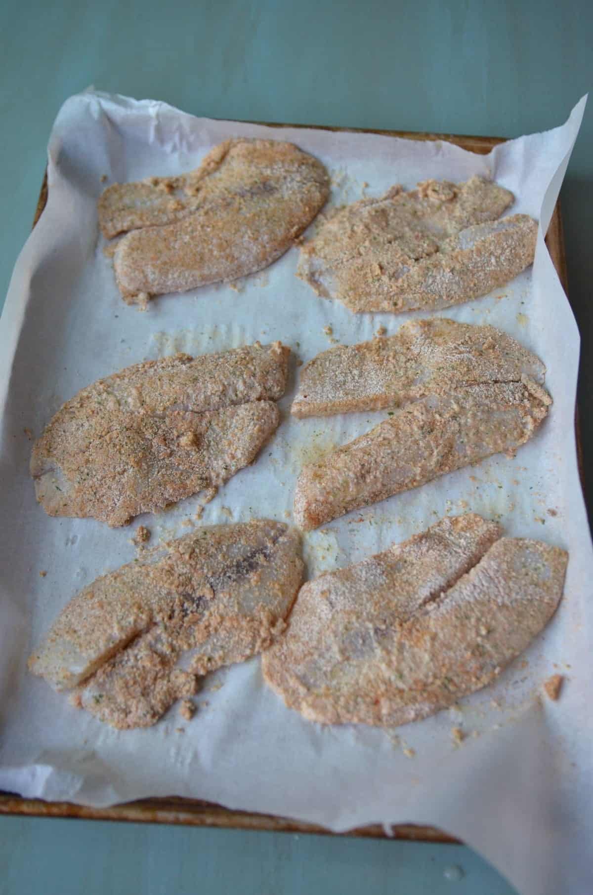 Parchment lined sheet pan with seasoned tilapia.