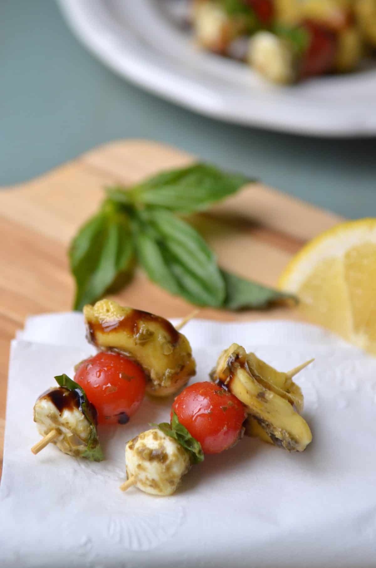 Two tortellini Caprese Skewers on a cutting board with lemon and basil leaves