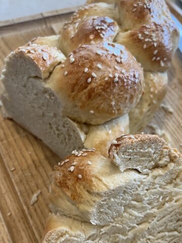 Six-strand challah bread on a cutting board with sesame seeds.