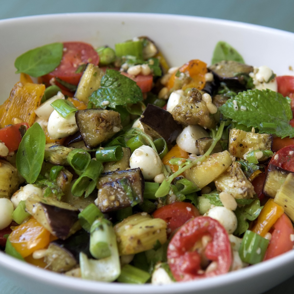 Roasted eggplant salad with tomatoes and cheese in a white bowl.