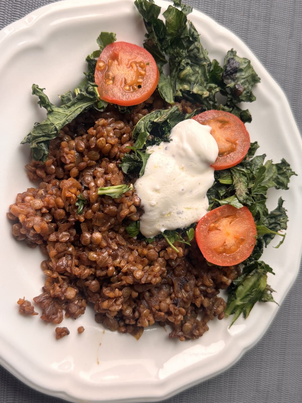 Mujadara hamra with lentils, bulgur, and caramelized onions, topped with tomatoes, toasted kale, and garlic yogurt sauce.